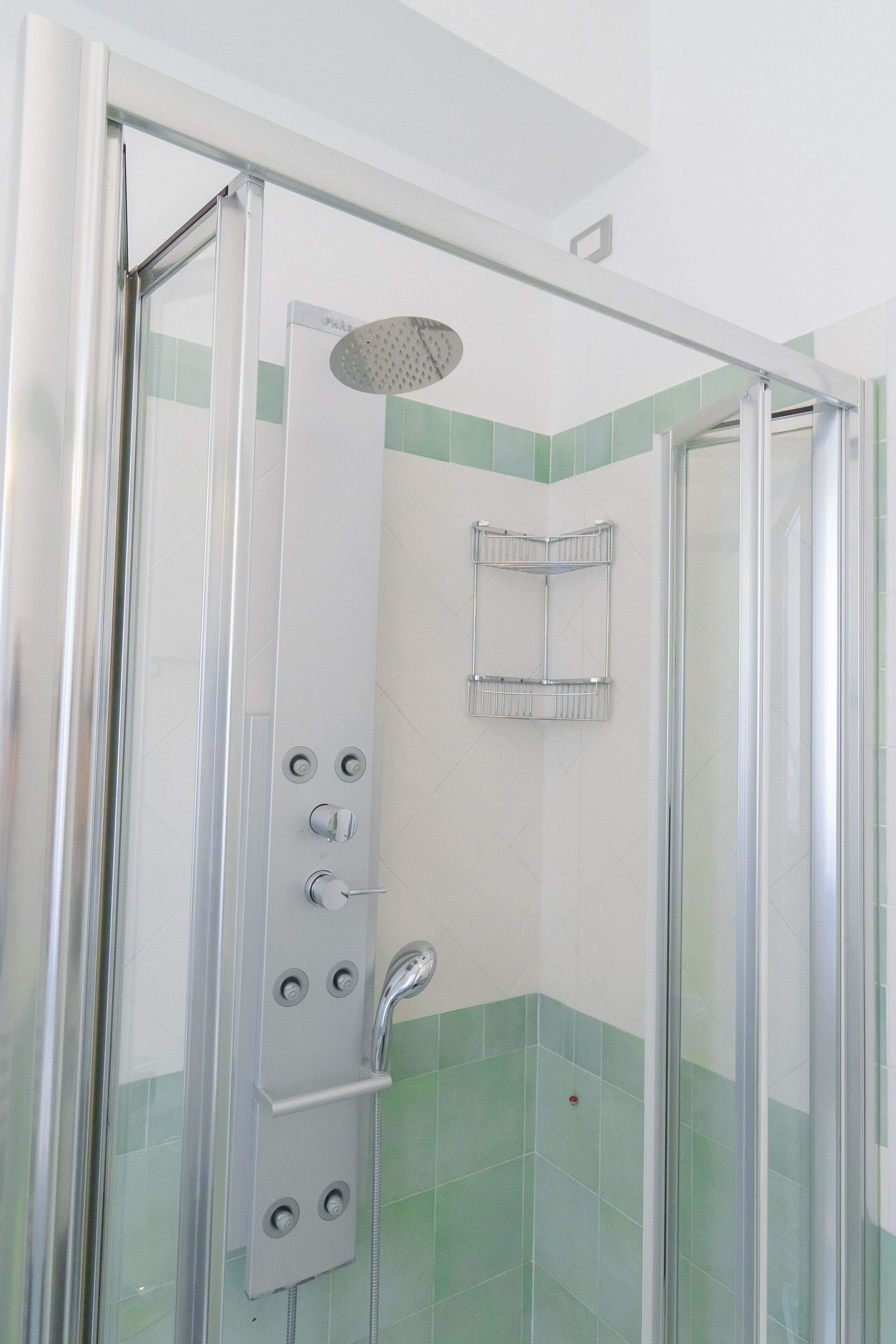 Ducha con cerramiento de vidrio, cabezal de ducha de mano, toallero empotrado y diseño de azulejos en esquina.
