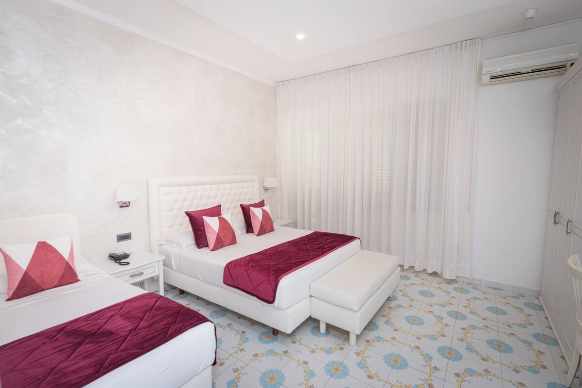 Une chambre d’hôtel avec un lit, une table de chevet et un petit banc.