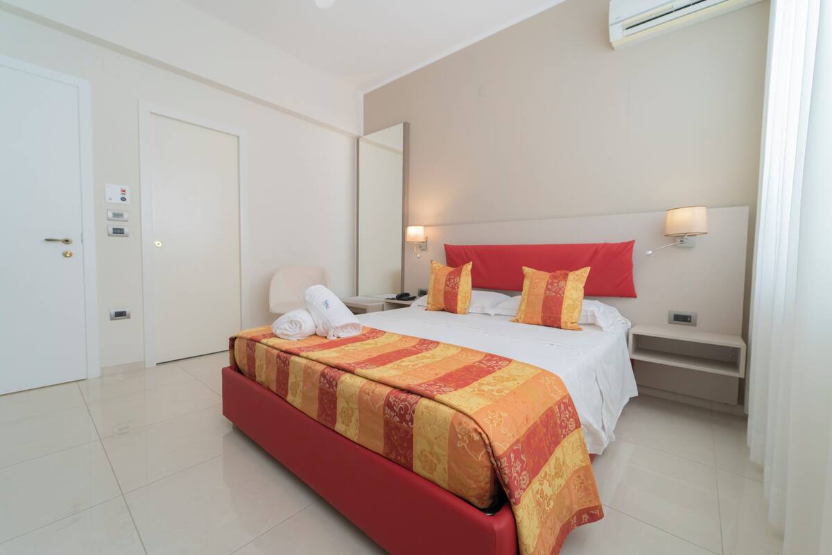 Une chambre d’hôtel avec un lit, une table de chevet, une chaise et une porte.