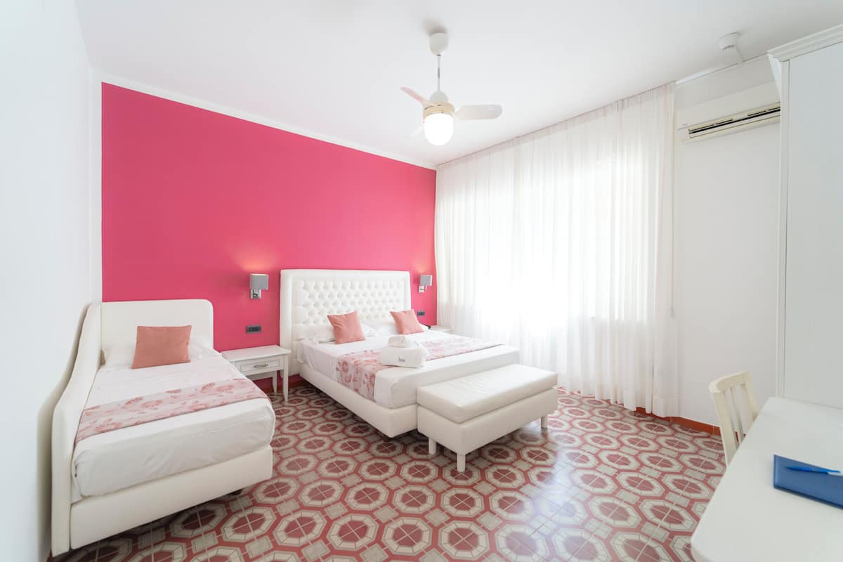 A bedroom with a white bed, a white bench, a ceiling fan, and a patterned floor.