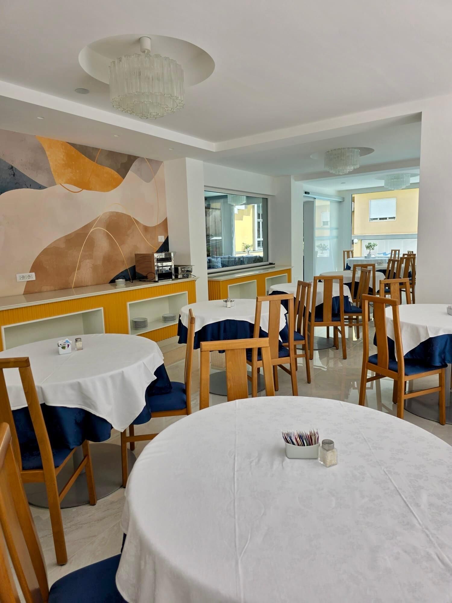 A dining area with round tables, chairs, and a modern chandelier.