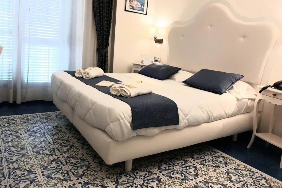 A neatly made bed with towels, a white headboard, a nightstand, and a picture on the wall.