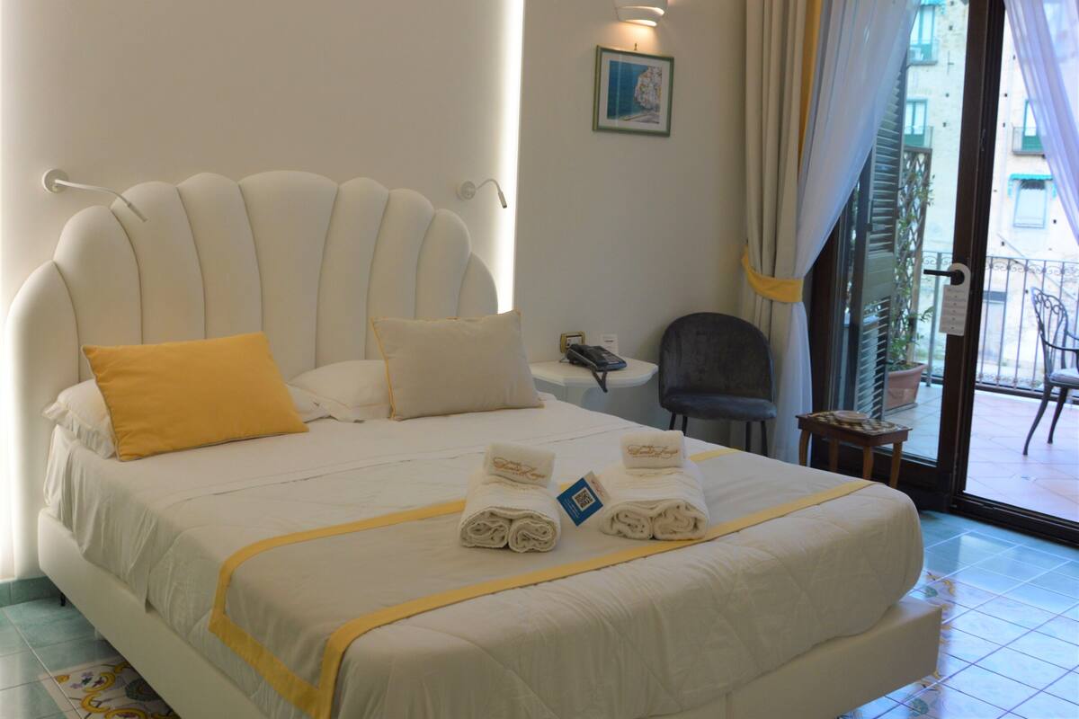 A hotel room with a large bed, a small table, a chair, and a view of the outside.