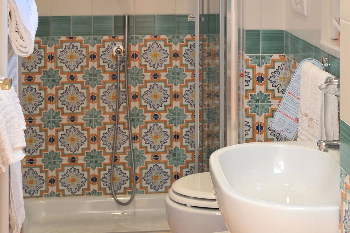 A bathroom with a shower, toilet, and sink, featuring patterned tiles and a tiled floor.