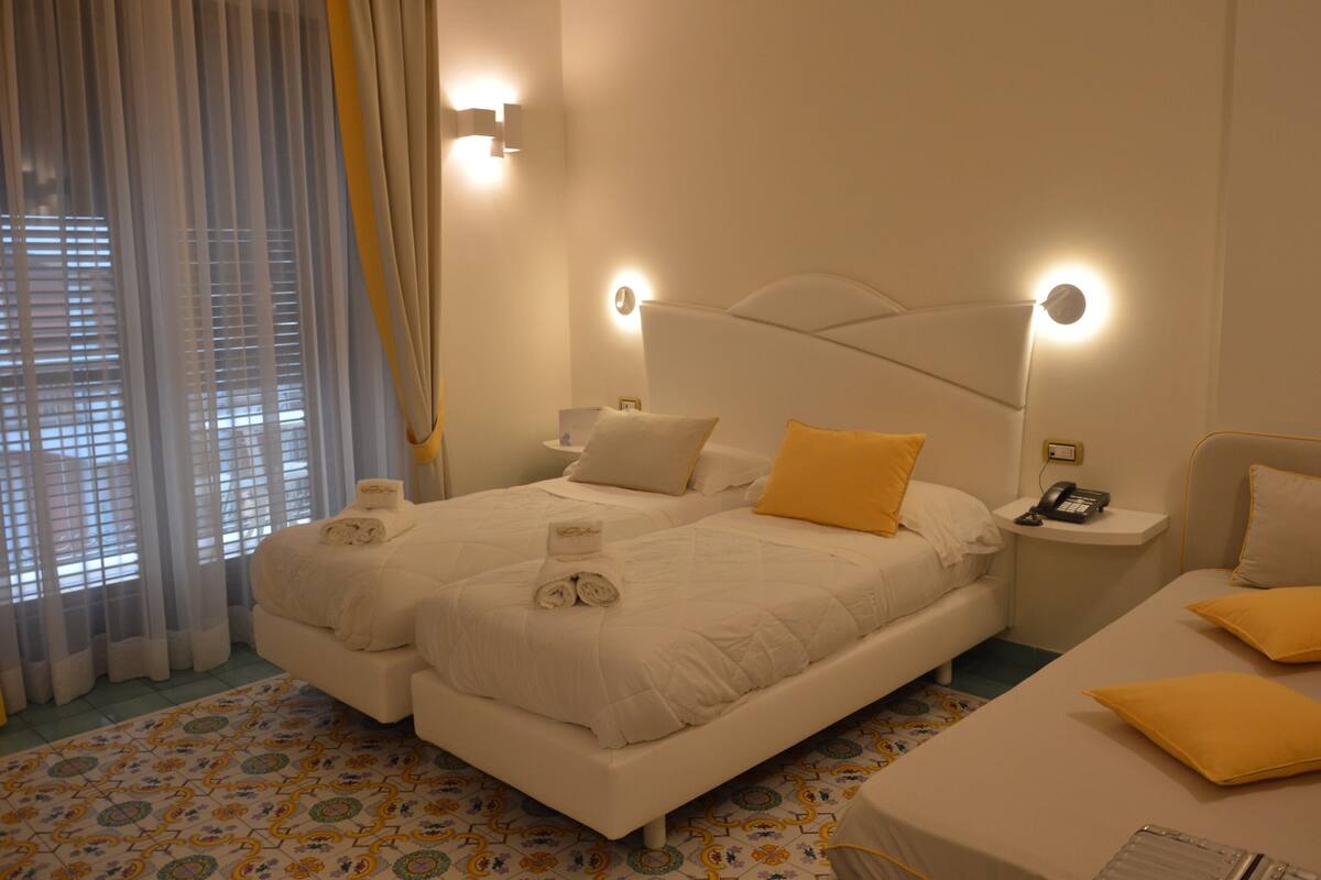 A hotel room with two beds, a bedside table with a phone, and a window with curtains.