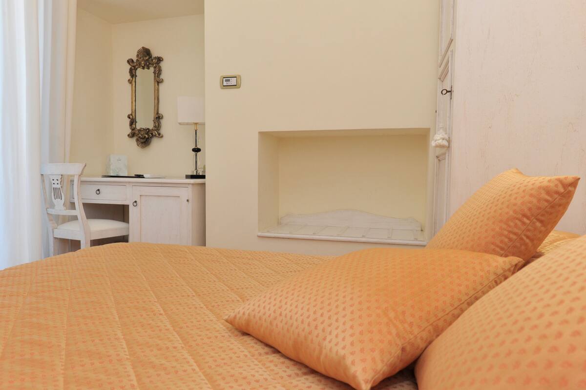A bedroom with a bed, a desk, a chair, a mirror, and a shelf.