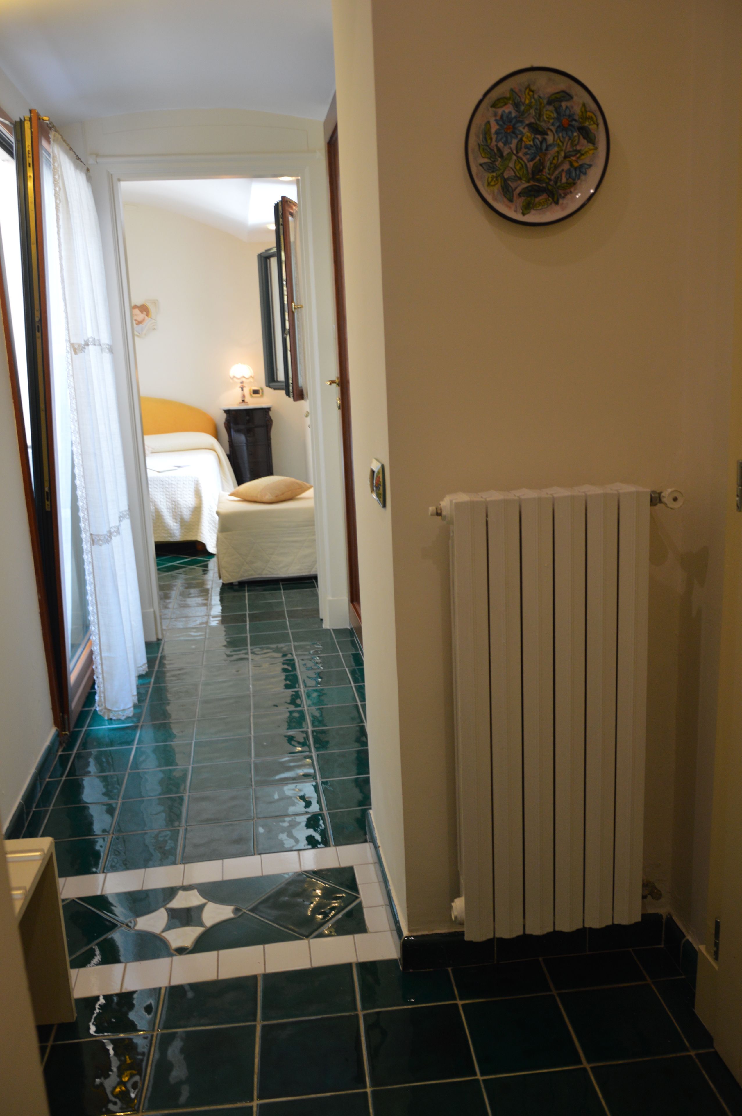 A narrow hallway with a radiator, a bed with a white headboard, and a door leading to another room.