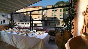 A table set with various dishes and drinks, a large terracotta pot, and a decorative lion head sculpture. - Hotel Santa Lucia (Minori)