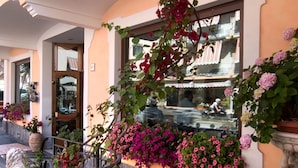 A hotel entrance with a curved balcony, potted plants, and a tiled floor. - Hotel Santa Lucia (Minori)