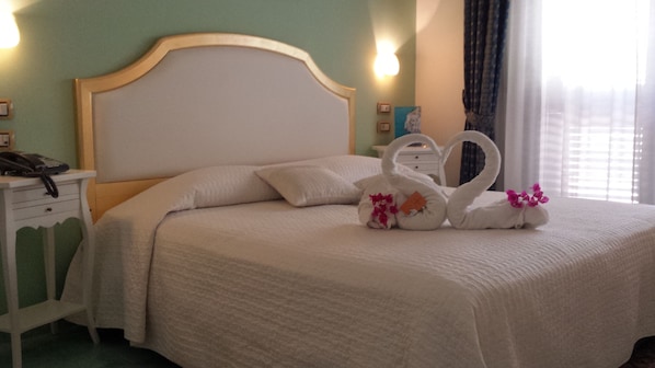 A neatly made bed with white linens, a wooden headboard, and decorative swans with flowers.