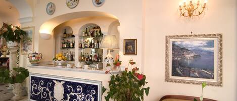 Un espace bar avec un présentoir pour les vins et les spiritueux, un mur décoratif agrémenté d’un tableau encadré et un lustre.