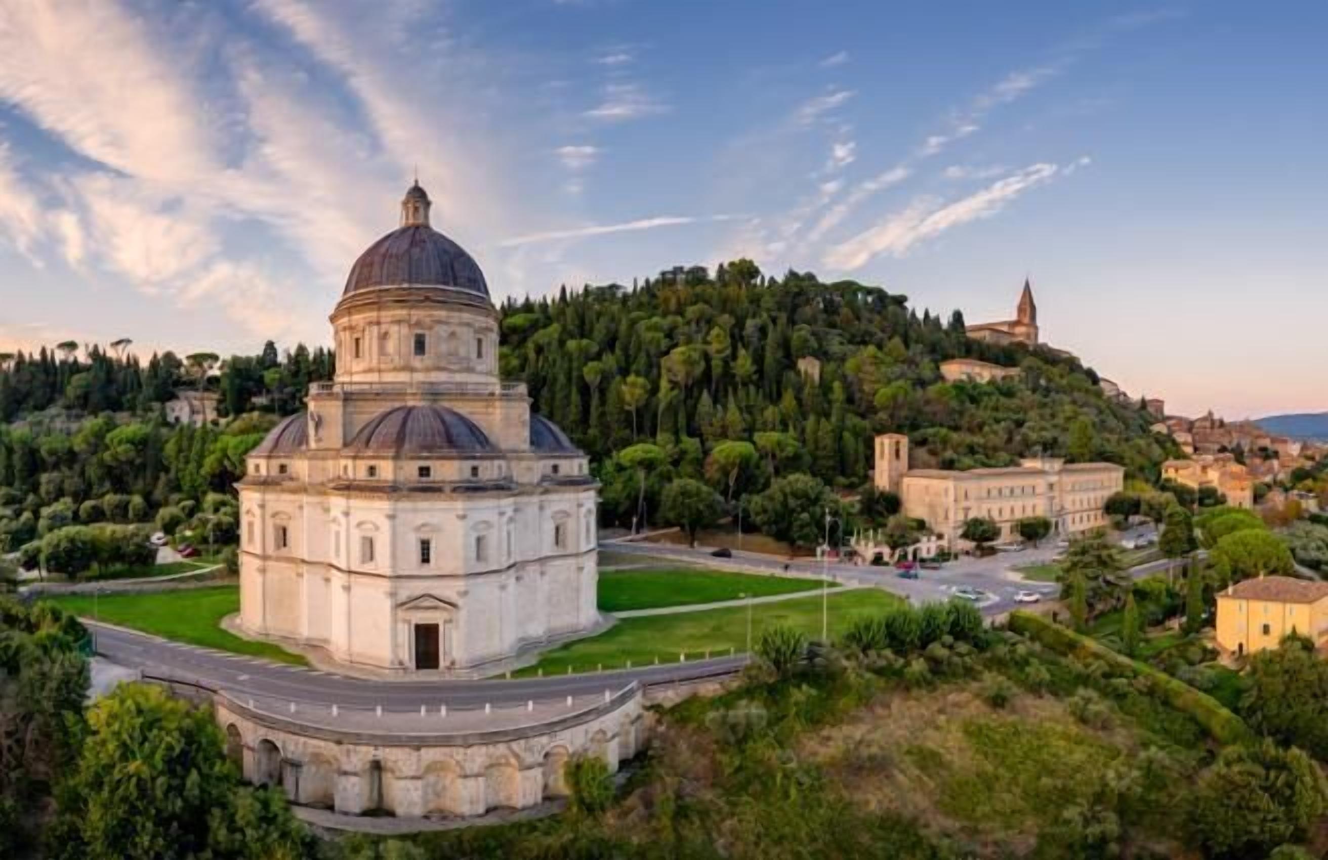 Un bâtiment historique surmonté d’un dôme, entouré d’une végétation luxuriante et adossé à une colline où se trouve une église.