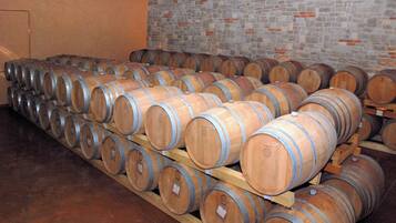 Des barriques en bois, empilées sur des palettes en bois, se trouvent dans une pièce dont un des murs est en pierre.