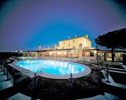 Una gran piscina al aire libre rodeada de una terraza de piedra, con un edificio al fondo.