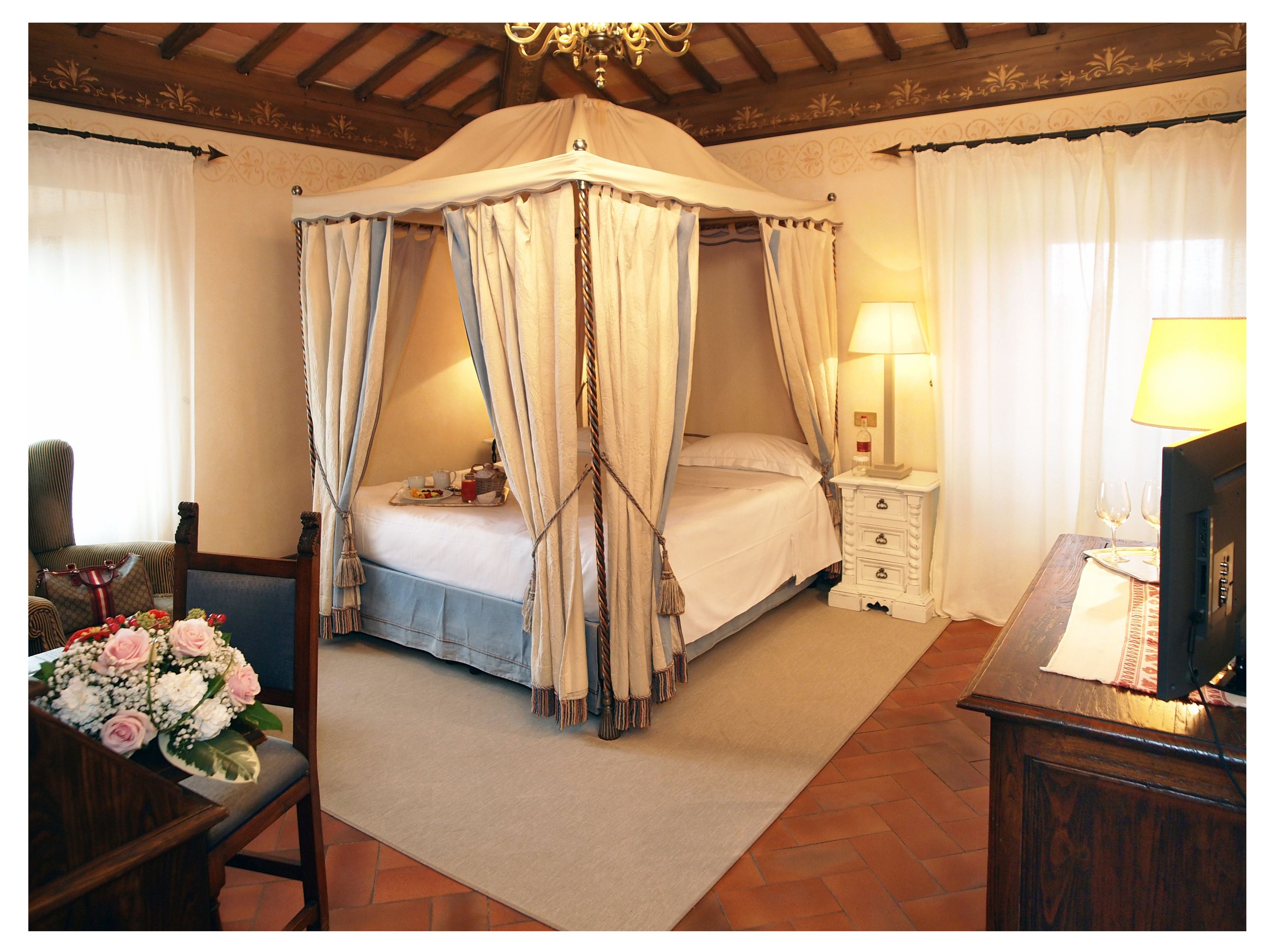 A bedroom with a four-poster bed, a nightstand with a lamp, and a wooden desk with a chair.