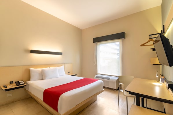 Una habitación de hotel con cama, mesita de noche, escritorio, silla y ventana.