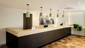 A reception desk with a light wood finish, a dark counter, and green pendant lighting. - City Express by Marriott Cancun (Cancun)