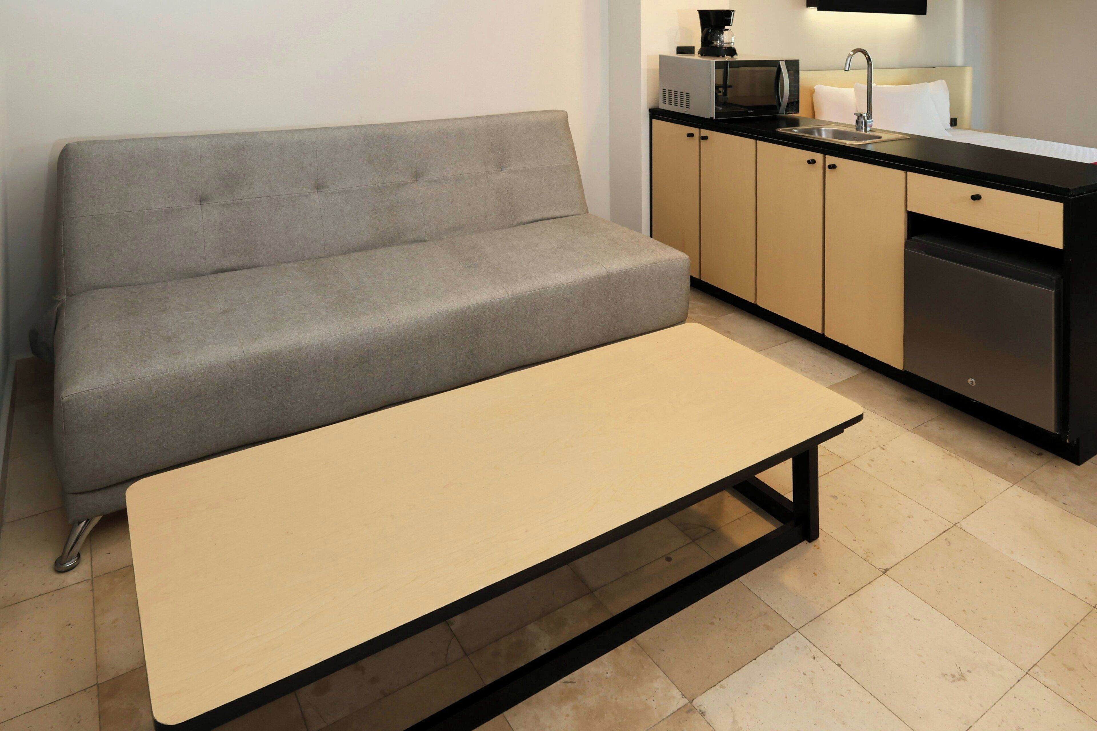 Una kitchenette moderna con un sofá gris, una pequeña mesa de comedor y un microondas.