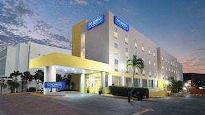 A hotel with a modern design, featuring a prominent entrance with a sign, a covered walkway, and a parking area. - City Express by Marriott Cancun (Cancun)