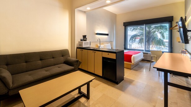 A compact living space with a sofa, a dining table, a kitchenette, and a bed. - City Express by Marriott Cancun (Cancun)