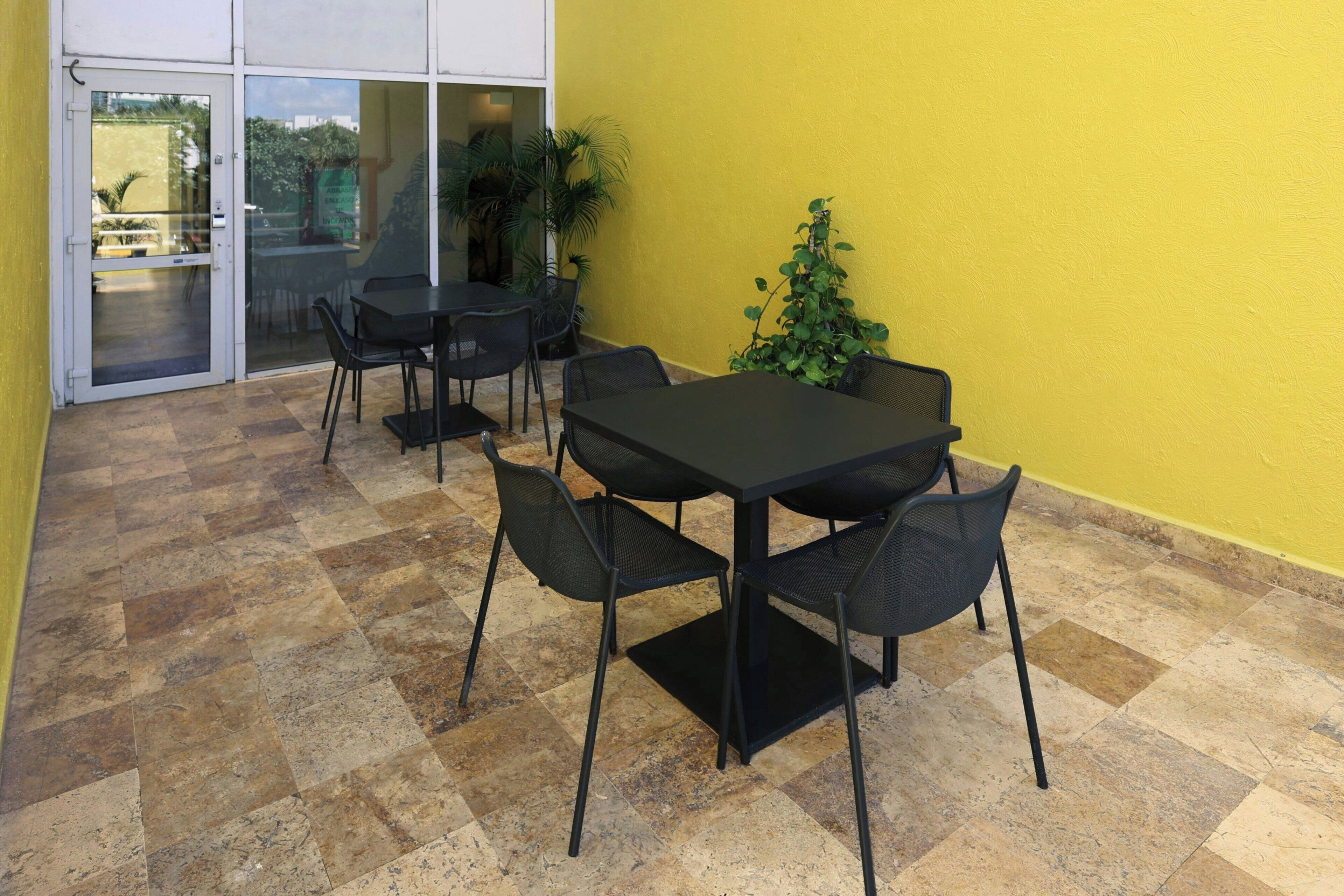 An outdoor patio with a table and chairs, a yellow wall, and a glass door leading to an interior space.