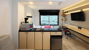 A modern kitchen with a central island, a dining area with a chair, a flat-screen TV mounted on the wall, and a window with blinds. - City Express by Marriott Cancun (Cancun)