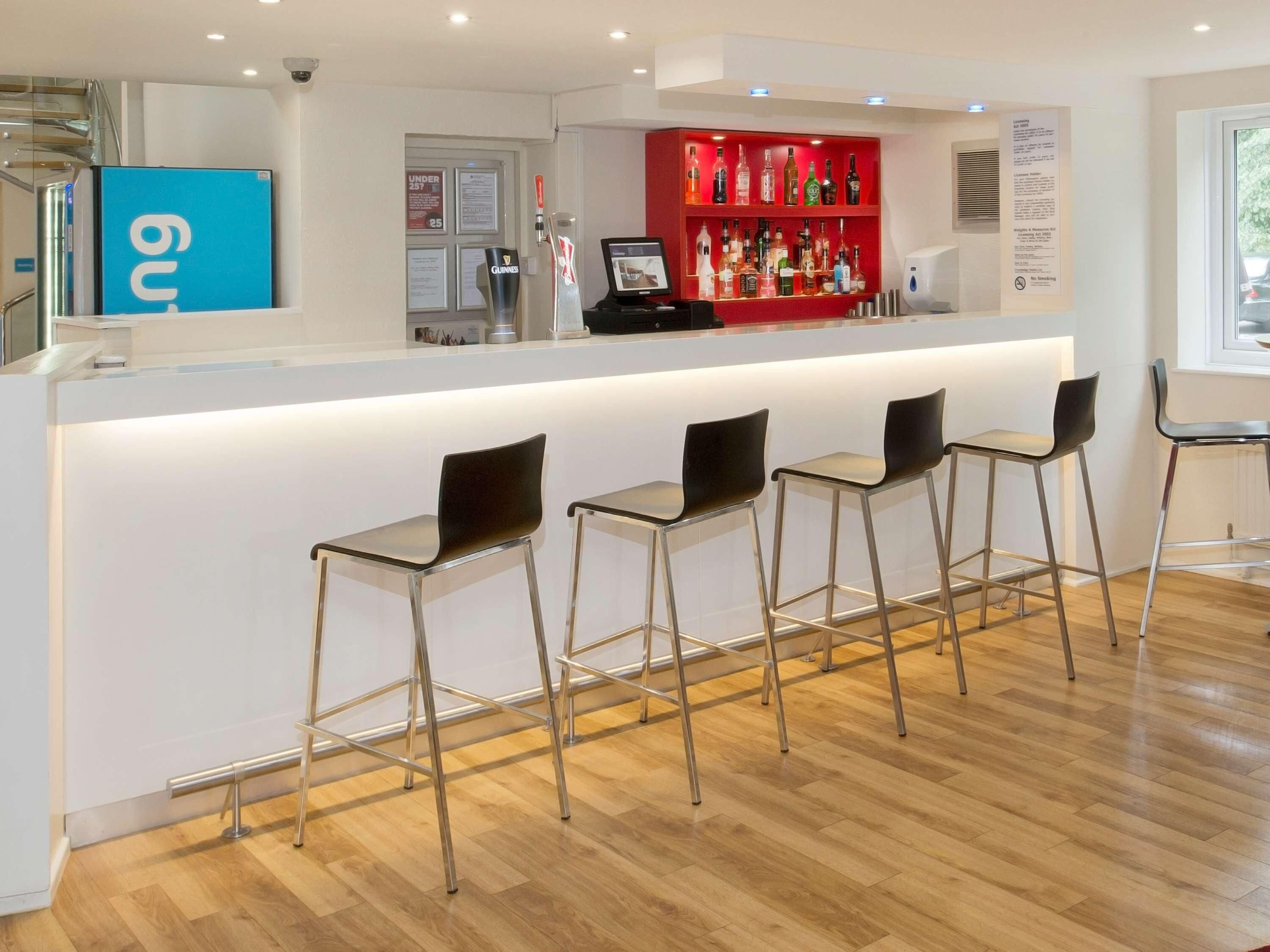 Zona de bar con mostrador, taburetes y una estantería roja para licores.