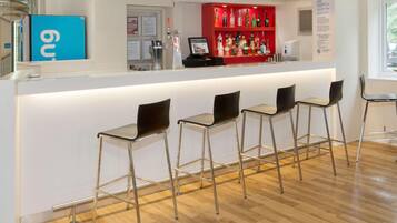 Zona de bar con mostrador, taburetes y una estantería roja para licores.