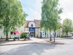 A Travelodge hotel with a sign, picnic tables, and a parking area. - Travelodge Manchester Sportcity (Manchester)
