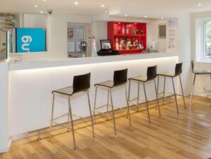 A bar area with a counter, stools, and a red liquor shelf. - Travelodge Manchester Sportcity (Manchester)