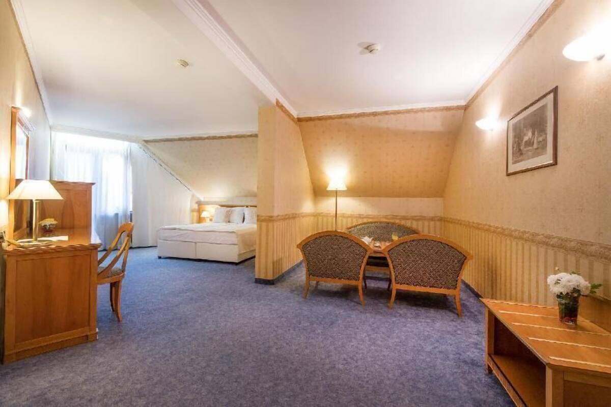 A hotel room with a sofa, two chairs, a small table, a desk, and a lamp.
