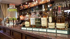 A bar counter with various bottles of liquor, including brands like Talisker and Lagavulin, displayed on a wooden counter with a glass display case. - Hotel Downtown (Sofia)