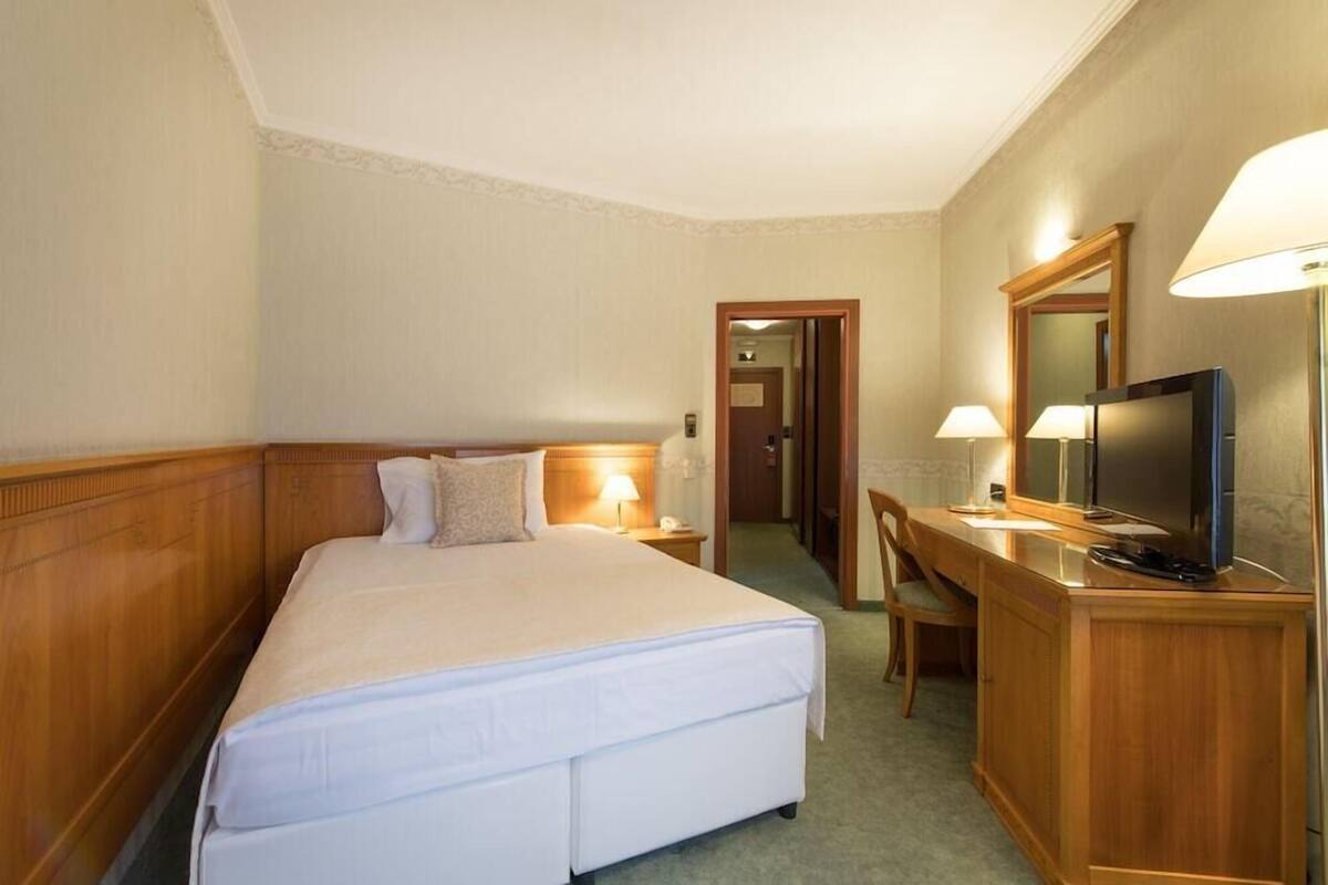 A hotel room with a bed, bedside lamps, a desk with a television, and a mirror.