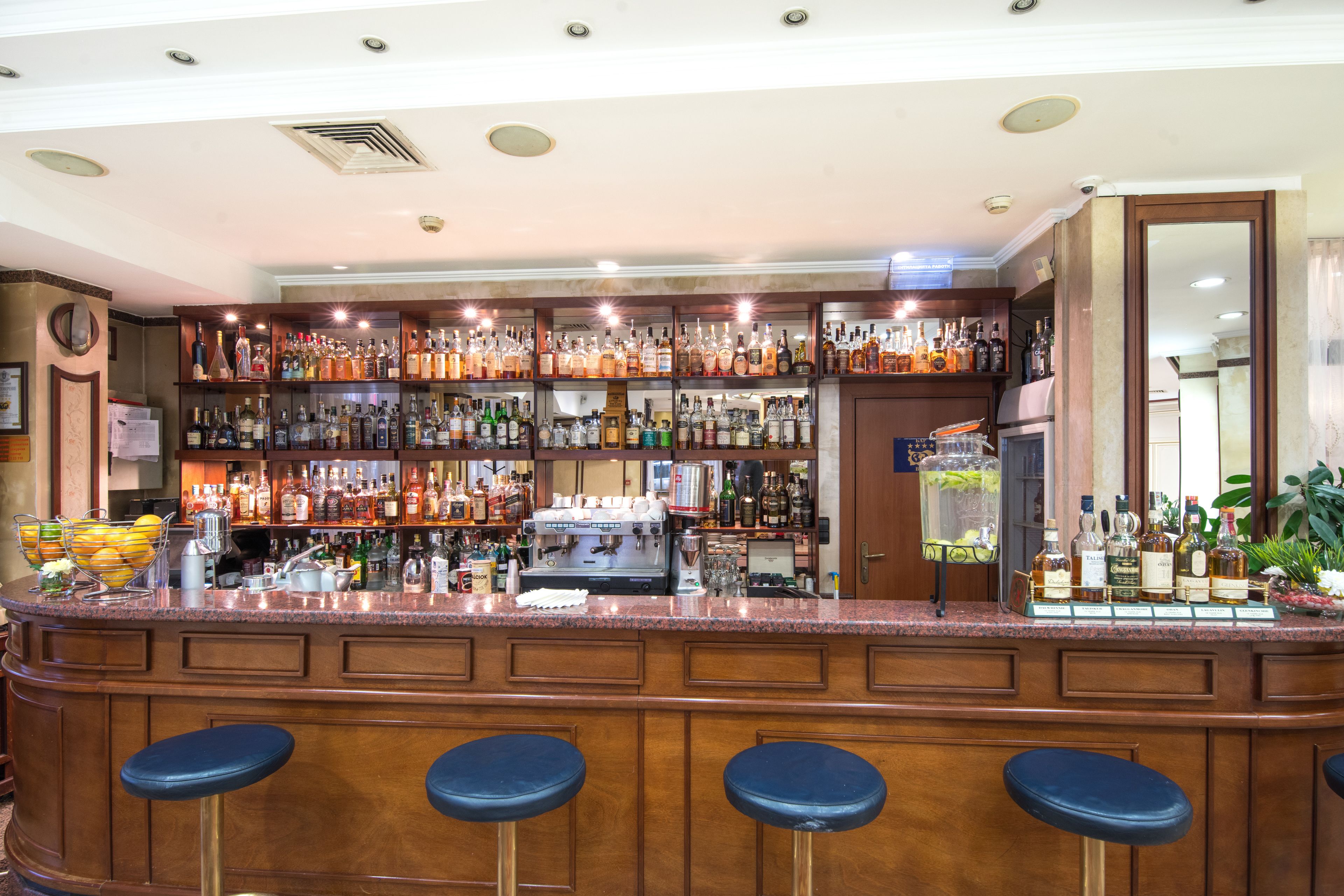 A bar area with multiple shelves of liquor bottles, a coffee machine, and four bar stools.