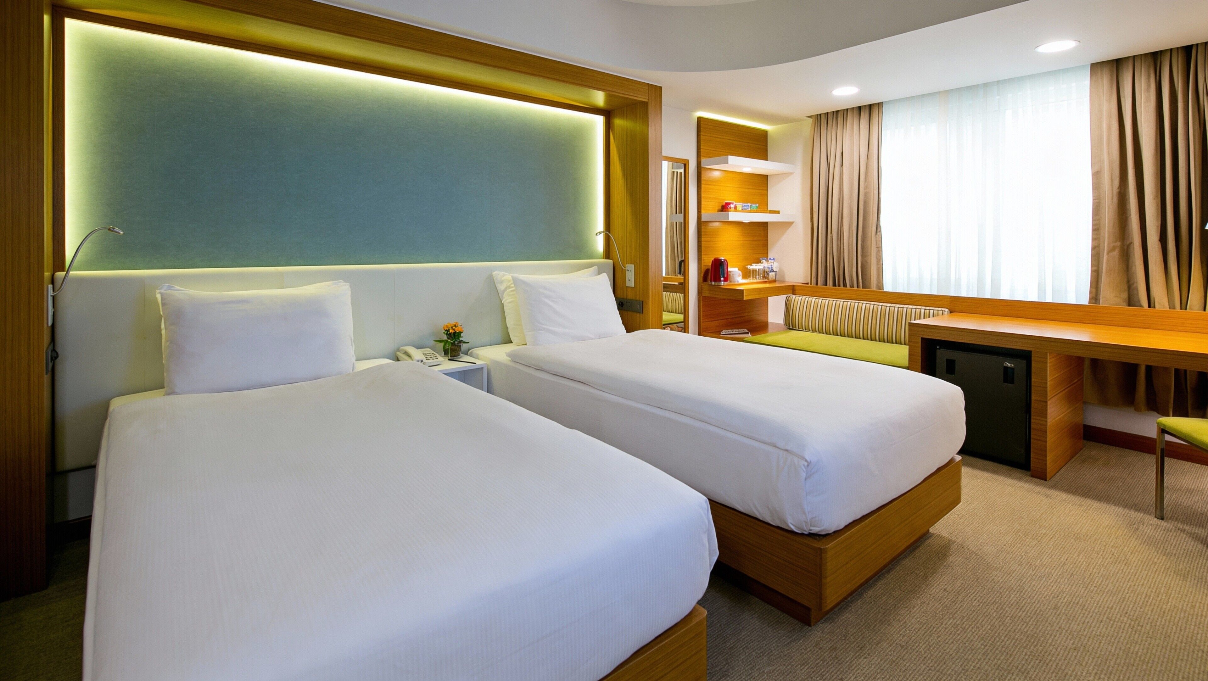 A hotel room with two beds, a desk, a chair, a small refrigerator, and a bathroom with a shower.