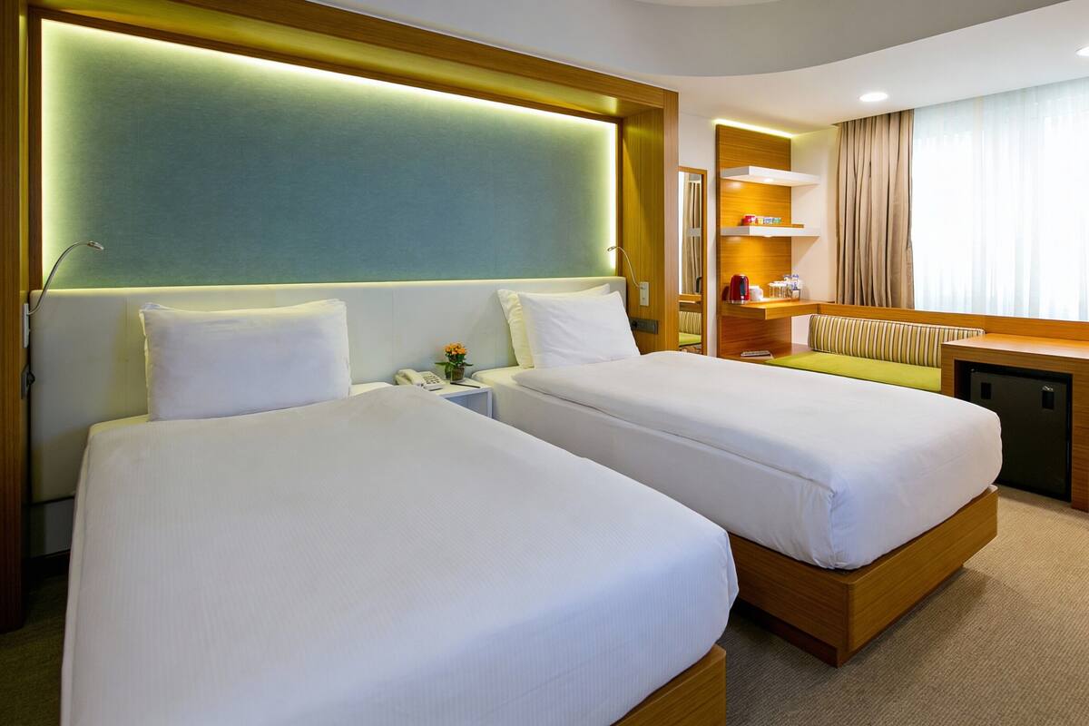 Habitación de hotel con dos camas, un escritorio, una silla, un refrigerador pequeño y un baño con ducha.