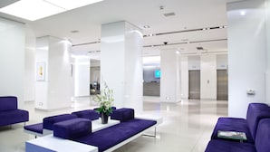Een moderne lobby met paarse zitplaatsen, een receptiebalie en een strak, wit interieur.