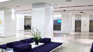 Een moderne lobby met een zithoek, bestaande uit een witte tafel en blauwe banken, een potplant en een receptiebalie op de achtergrond.