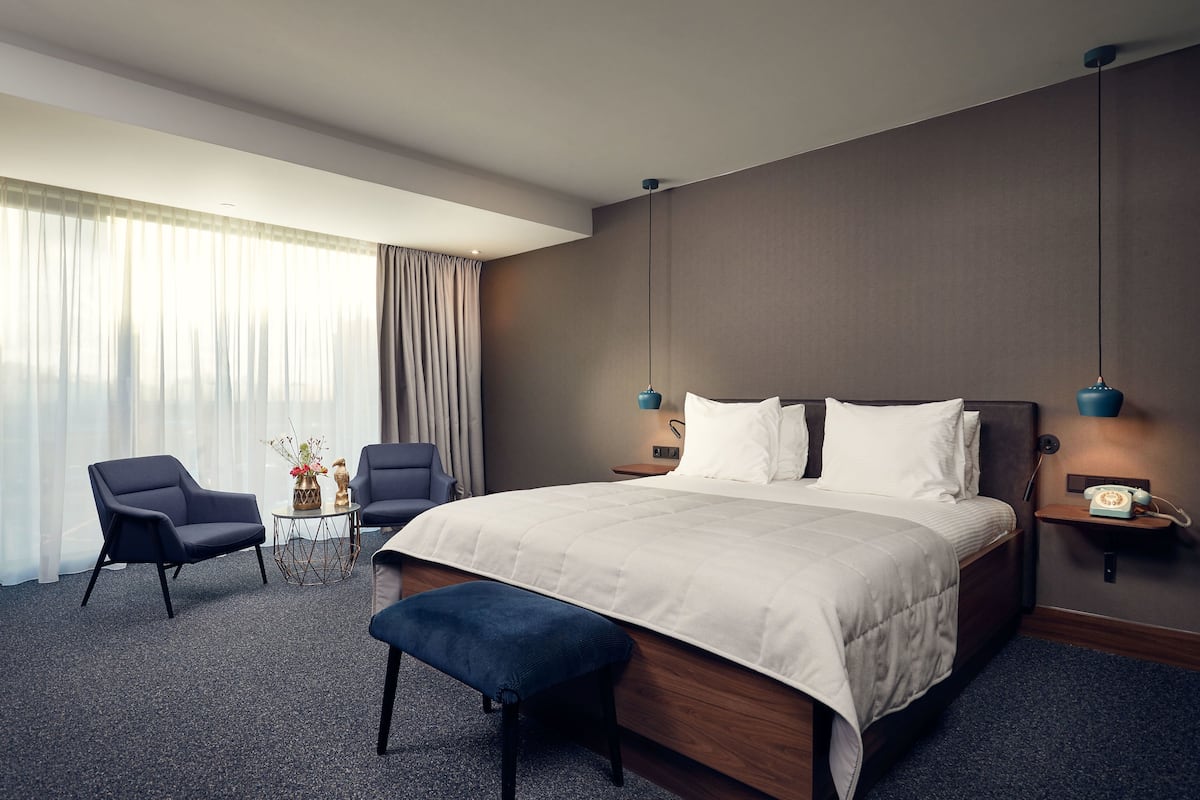 Ein modernes Hotelzimmer mit einem großen Bett, zwei Sesseln, einem kleinen Tisch mit einer Vase und einem Nachttischtelefon.