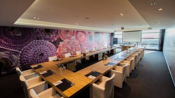 A conference room with a long table, white chairs, and a large screen.