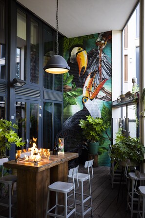 Zona de bar con un mural de tucanes, barra de madera y asientos.