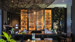 Un espace bar doté d’un grand lustre rond au centre, d’étagères remplies de bouteilles et d’un coin salon.