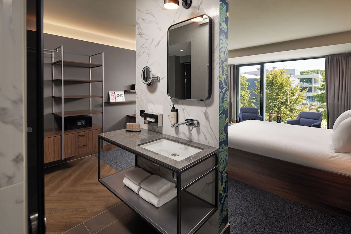 Ein modernes Hotelzimmer mit Marmorbad, einem großen Bett, Blick auf die Stadt und einer eingebauten Ablage mit Handtüchern.