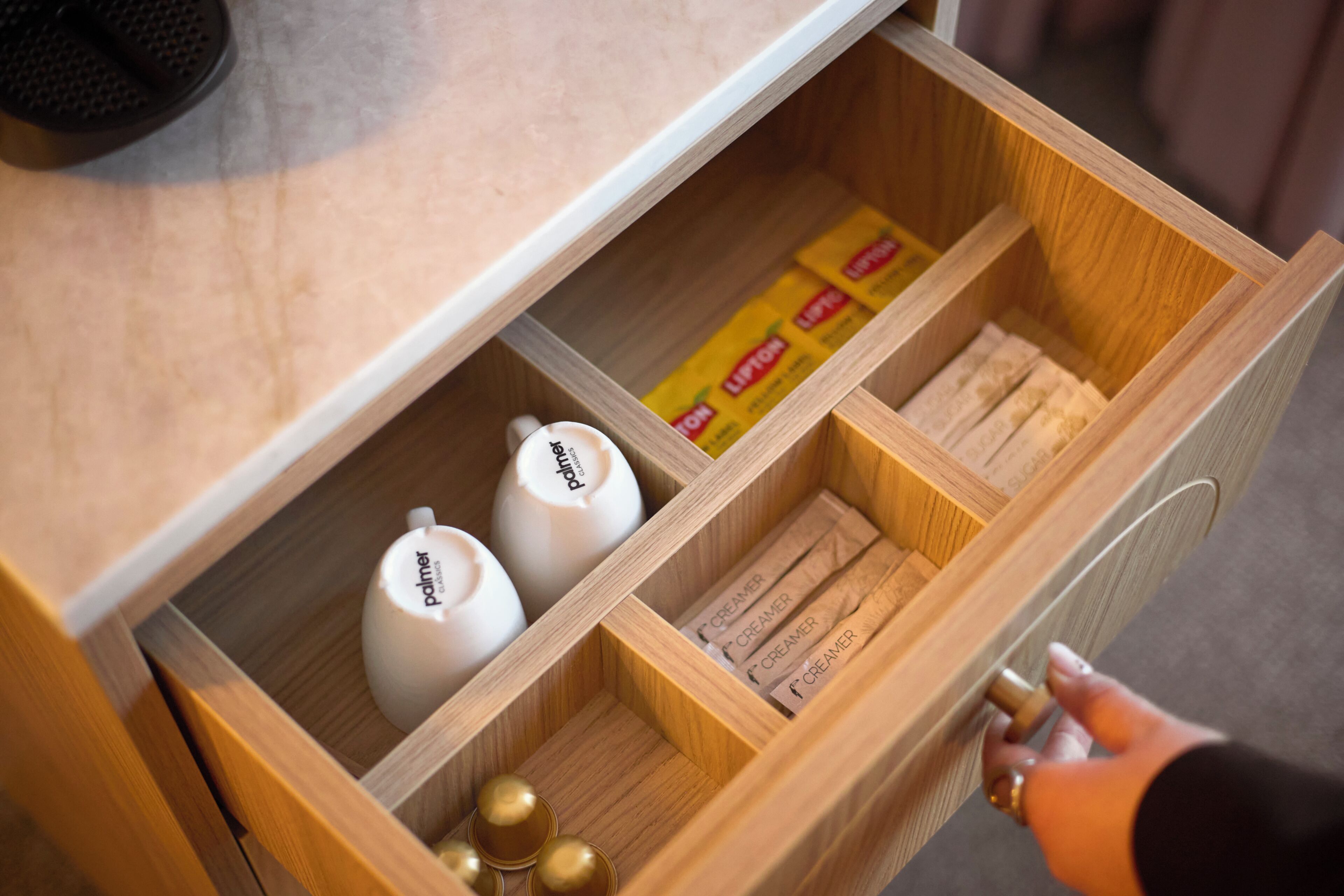 Un cajón de madera con compartimentos que contienen artículos de aseo personal y una caja de té Lipton.