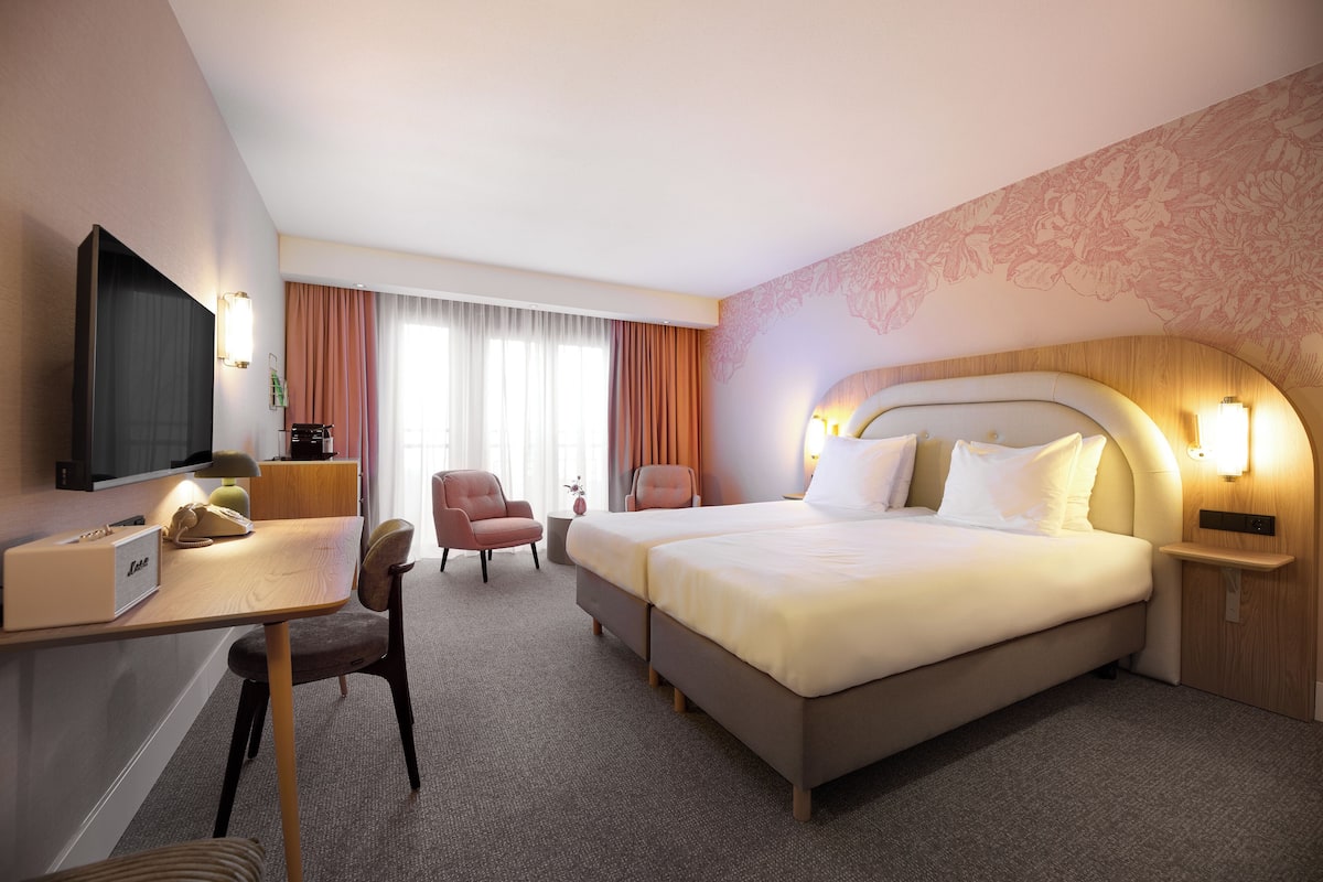 Ein Hotelzimmer mit einem großen Bett, einem Schreibtisch, einem Flachbildfernseher, einem Sessel und einem kleinen Tisch.