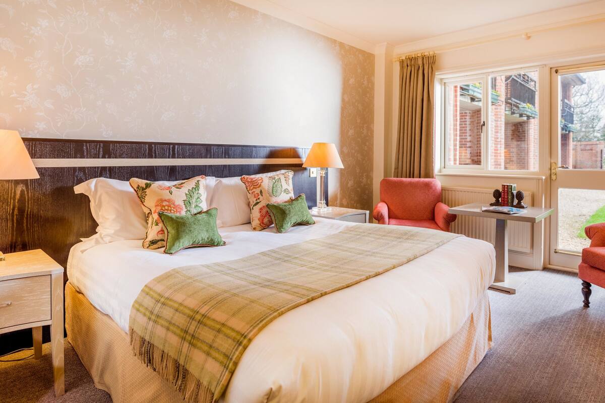 A hotel room with a large bed, two bedside tables, a desk, a chair, and a window with curtains.