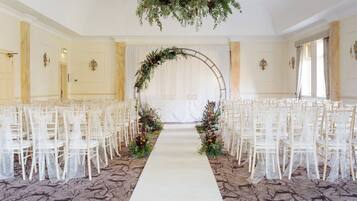 Un pasillo nupcial con sillas blancas a ambos lados, una alfombra blanca y decoración floral.