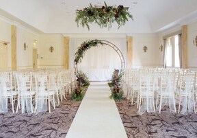 Un pasillo nupcial con sillas blancas a ambos lados, una alfombra blanca y decoración floral.