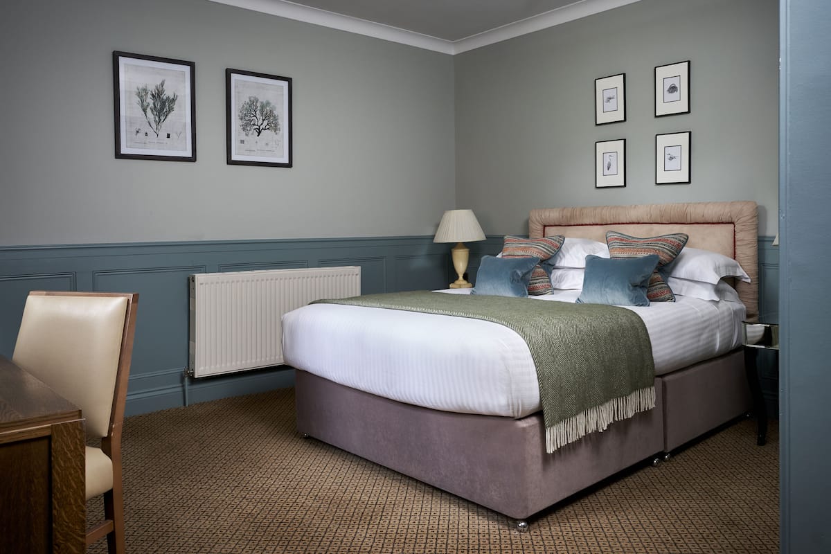 A bedroom with a bed, a chair, a lamp, and framed botanical prints on the wall.