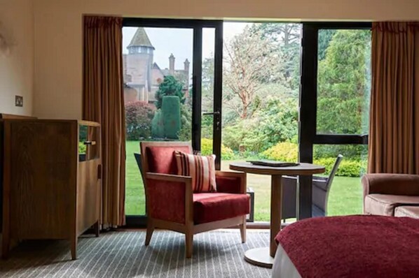A hotel room with a large window, a red armchair, a round table, and a bed. - Careys Manor & Senspa (Brockenhurst)